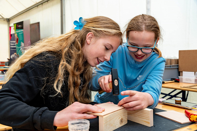 Zwei Mädchen arbeiten gemeinsam an einem Holzprojekt bei einem Explore-Science-Workshop und haben sichtlich Spaß dabei.